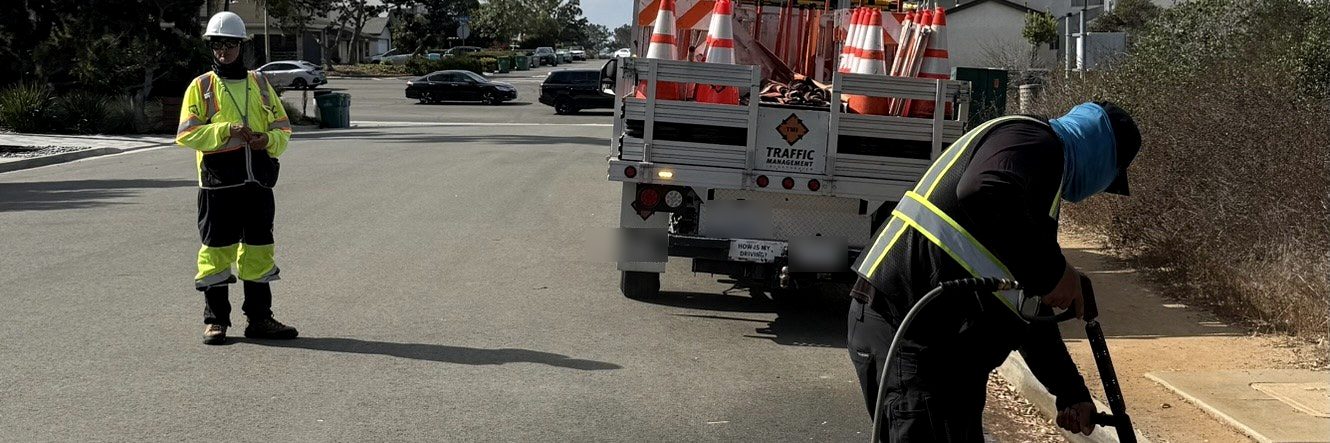 Crew member pressure washing a curb line while a flagger and a traffic control truck hold the lane