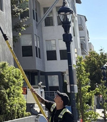 Technician cleaning upper-floor windows of a mid-rise building with a water-fed pole